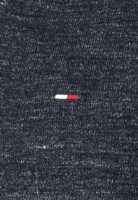 Tissu tricoté bleu foncé avec un petit détail rectangulaire horizontal en fils blancs et rouges près du centre.