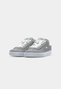Grijze suède sneakers met witte veters en rubberen zool, voorzien van een groen-geaccentueerd logo op de tong en een slank, minimalistisch ontwerp.
