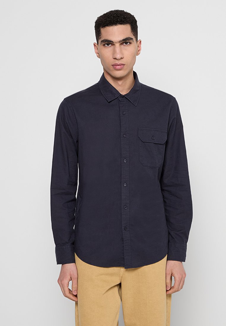 Marineblauw overhemd met lange mouwen van katoen, voorzien van een knoopsluiting kraag, een voorkant zak en een gestructureerde stof, gecombineerd met beige broek.