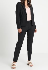 Svart skräddarsydd kavaj, rosa v-ringad topp, svarta smala byxor och vita sandaler med guldaccenter. Slät tygkvalitet, strukturerad design, åtsittande silhuett.