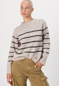 Beige knitted sweater with black horizontal stripes, crew neckline, and ribbed cuffs, paired with khaki cargo pants.