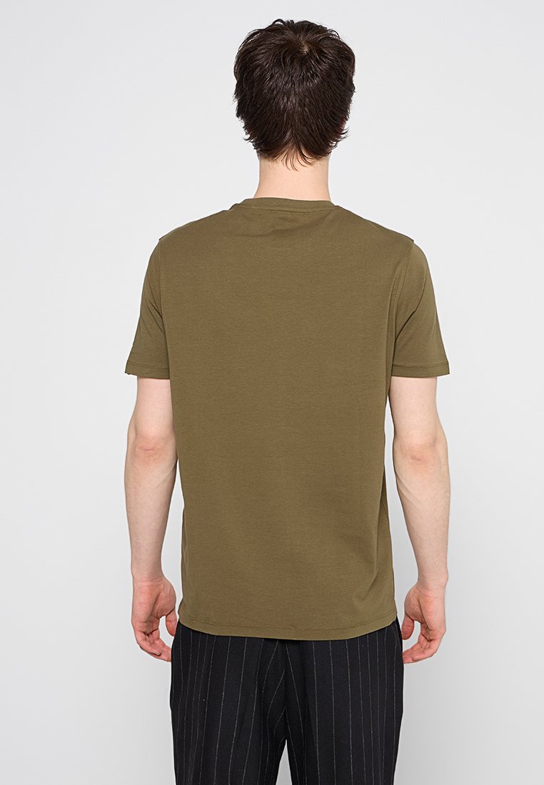 Olivgrünes Baumwoll-T-Shirt mit kurzen Ärmeln und rundem Halsausschnitt. Glatte Textur, taillierte Passform, von hinten betrachtet. Gestreifte schwarze Hose.