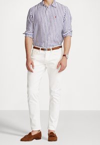 Randig skjorta i blått och vitt, vita slim-fit byxor, brunt läderbälte och loafers, klocka på handleden. Snygg, åtsittande design.