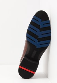 Semelle de chaussure en cuir marron avec une base en caoutchouc noir, ornée de motifs en zigzag bleus et d'un accent rouge près du talon. Surface texturée.