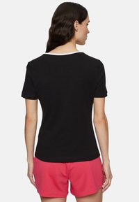Zwart T-shirt met korte mouwen en een ronde halslijn, afgewerkt met witte bies. Zachte stof met een gladde textuur, gedragen met roze shorts.