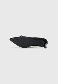 Chaussure à talon haut en suede noir avec un bout pointu et un talon fin. La semelle est lisse avec un logo discret sur le dessous.