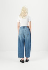 Jeans de ganga azul de perna larga com uma cintura alta, apresentando bolsos traseiros e um retalho de pele. Combinados com uma t-shirt justa de malha branca.