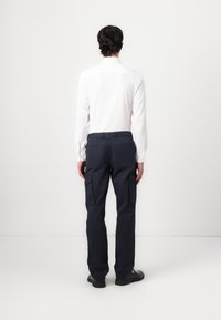 Witte lange mouwen overhemd voor heren, marineblauwe cargobroek met zijzakken, recht model, gladde structuur, gedragen met zwarte schoenen.