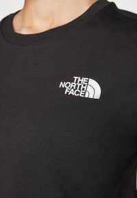 Fekete pamut póló, kerek nyakkivágással; az elején fehér "The North Face" logónyomattal.