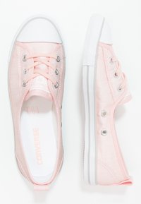 Zapatillas de lona rosas de corte bajo de Converse con punteras y suelas de goma blanca, ojetes de metal y cordones rosas, mostradas en vistas superior y lateral.