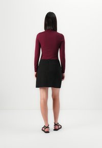 Haut bordeaux à manches longues associé à une jupe noire longueur genoux ; tissu lisse, design ajusté et accents minimalistes. Des sandales noires complètent le look.