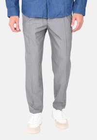 Pantaloni grigi su misura con una texture liscia, caratterizzati da una vestibilità dritta e sottili righe verticali, abbinati a sneaker bianche.