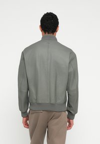 Harmaa nahkainen pommitakki, jossa on resorikaulus ja -hihansuut, sileä pinta ja minimalistinen muotoilu. Tasainen takaosa.