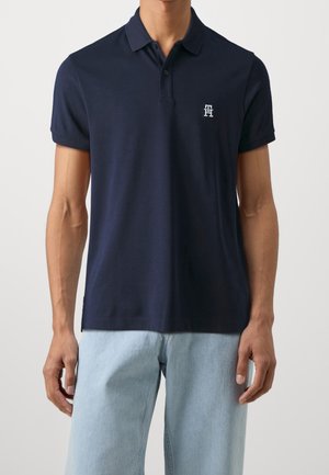 Polo-shirt marine en coton avec un col classique, des manches courtes et un petit logo de marque sur la poitrine gauche. Il possède un ourlet droit.