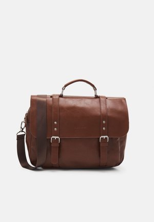 Brown leather satchel bag with buckled straps, top handle, and detachable shoulder strap on a light background.