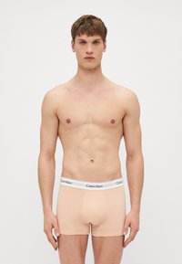 Calvin Klein férfi boxer alsónadrág világos őszibarack színben, fehér márkázott derékvonallal. Az anyag simának és testhezállónak tűnik, kiemelve a törzset.