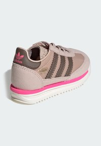 Teniska Adidas s béžovým a hnedým zvrškom, tromi tmavými pásmi, ružovými akcentmi a textúrovaným pätovým dielom, s bielou podrážkou.