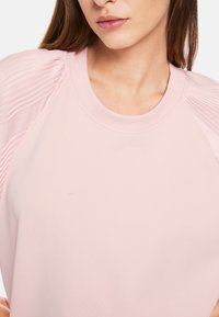 Helles rosa Sweatshirt mit gerippter Textur an den Schultern und Rundhalsausschnitt. Der Stoff wirkt weich und bequem.