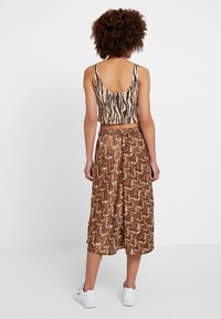 Avskuren tanktopp med zebramönster, kombinerad med en knälång kjol i brunt ormskinnsmönster, bärs med vita sneakers.