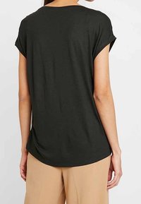 Tumma vihreä lyhythihainen paita, pehmeä kangas, rento malli, pyöristetty helma, näkyviä ompelutietoja hihoissa ja kauluksessa.