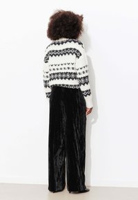 Pull en tricot blanc avec motifs géométriques noirs, associé à un pantalon large en velours noir. Texture douce, coupe décontractée.