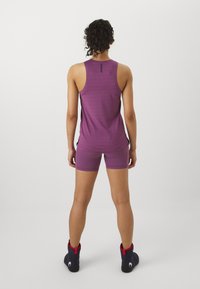 Violets krekls ar atbilstošajām biksēm, izgatavots no gludas auduma. Ir racerback dizains un sānu spraugas kustības brīvībai. Melna logo detaļa.