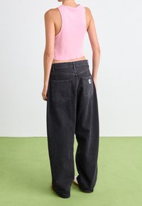 Zwarte wijde jeans met hoge taille en twee achterzakken, gecombineerd met een cropped roze mouwloze top. Platte zolen van schoenen zichtbaar.