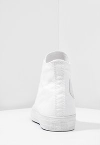 Baskets montantes en toile blanche avec une texture lisse, un bout rond, une semelle en caoutchouc et un patch logo circulaire sur le côté extérieur.