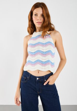 Horgolt crop top, amely hullámos mintázattal rendelkezik pasztell színekben (rózsaszín, kék, fehér), nyitott szövésű, sötétkék, magas derekú farmernadrággal párosítva.