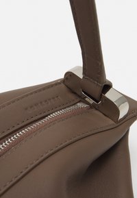 Brown leather handbag with a smooth texture, featuring a silver zipper and clasp, stitched detailing, and a single strap.
