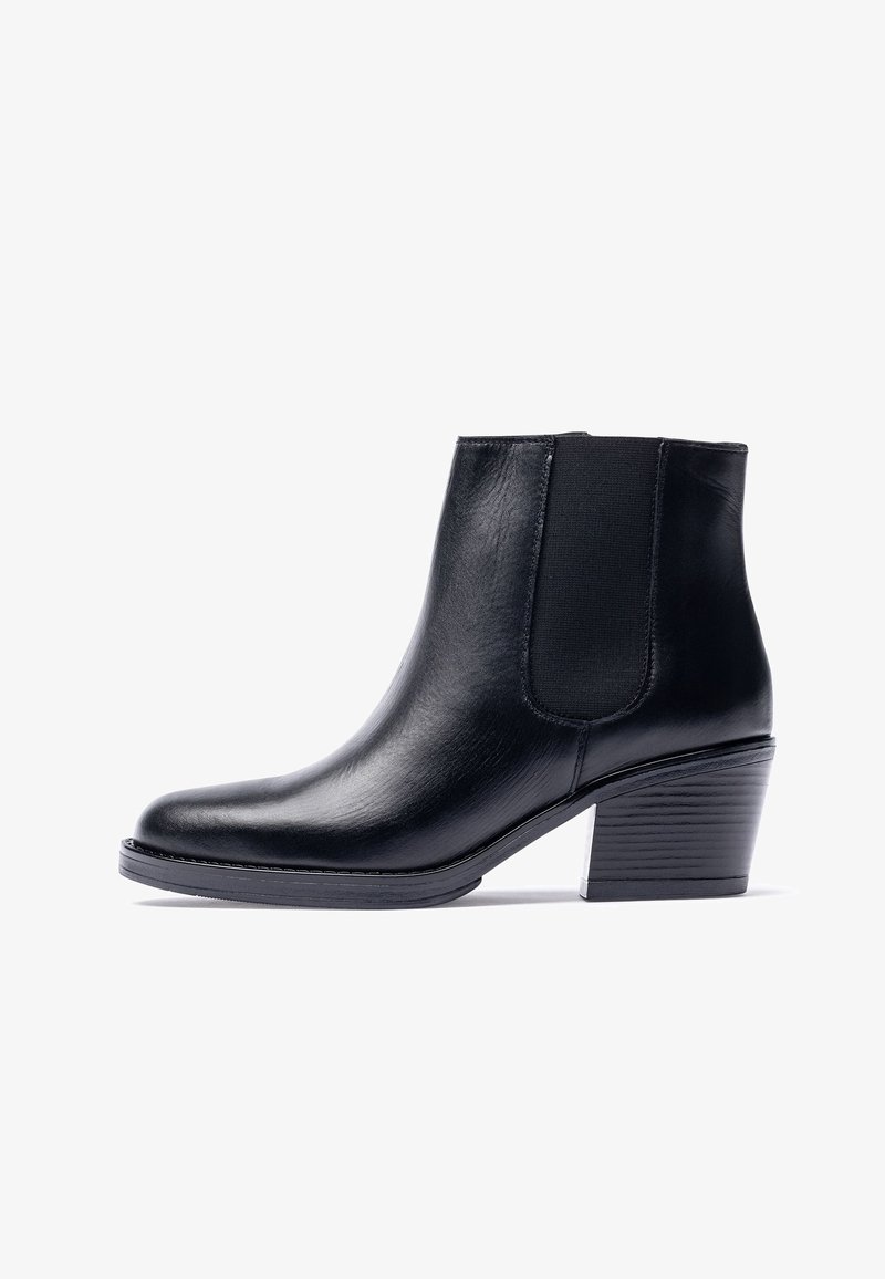 Botín de cuero negro con paneles laterales elásticos, puntera puntiaguda y tacón apilado. Textura suave con detalles mínimos de costura.
