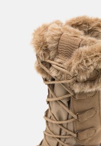 Stivali invernali beige con bordo in pelliccia, dettagli testurizzati e occhielli rinforzati per i lacci. Realizzati con materiali resistenti.
