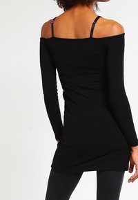 Top nero a coste con spalle scoperte e maniche lunghe, dotato di spalline regolabili e design aderente. Texture morbida e tessuto liscio.