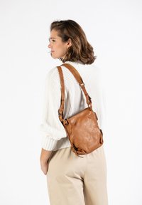 Bruine leren crossbody tas met een zachte textuur, verstelbare schouderband en minimalistisch ontwerp. Voorzien van een ritssluiting en subtiele hardware accenten.