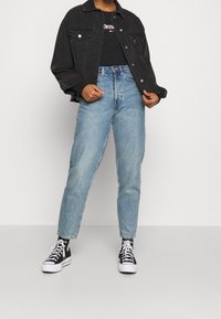 Svart jeansjacka, svart grafisk t-shirt, ljusblå högmidjade jeans och svarta högskaftade sneakers med vita sulor.