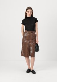 Melns īsām piedurknēm tops apvienots ar brūnu čūsku raksta ādas svārku ar priekšējo šķēlumu un zelta sprādzi. Modelis tur melnu rokassomu.