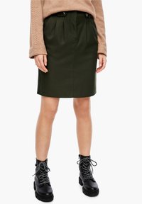 Jupe vert foncé, longueur genoux avec plis, dotée de poches avant et de boutons décoratifs. Portée avec des bottes de combat noires à lacets.