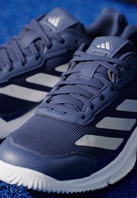 Niebieskie buty sportowe z teksturowanej tkaniny, tonowe sznurowadła i trzy odblaskowe białe paski po bokach, z białą gumową podeszwą.