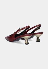 Zapatos de tacón de cuero burdeos con tiras al tobillo y puntera afilada, que cuentan con un tacón grueso con detalles en dorado y recortes laterales para añadir un detalle de diseño.