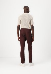 Kötött krémszínű pulóver, texturált paisley mintával, bordó slim-fit nadrággal és fehér sportcipővel párosítva, hátulról nézve.
