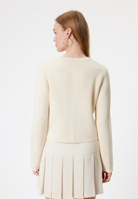 Crème-kleurige gebreide trui met lange mouwen, gestructureerde stof en een ronde halslijn, gecombineerd met een geplooide crème rok.
