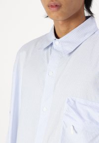 Light blue and white striped short-sleeve shirt, buttoned collar, front pocket, cotton material, smooth texture, subtle sheen.