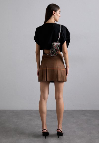 Must päikesevarju must cropped top lõhkemisega seljaosa, pruunis ruudulises mini seelikus on voldid ja väike ristseljakott, millel on mitmevärviline ruuduline muster.