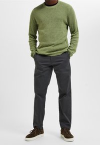 Groen getextureerd gebreid trui gecombineerd met grijze slim-fit broeken en donkere sneakers. De outfit heeft een casual ontwerp en eenvoudige kleuren.