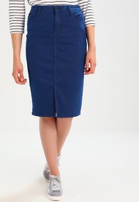 Mörkblå denim pennkjol med en framspringa, två fickor framtill och en figurnära silhuett. Kombinerad med grå sneakers och en randig topp.