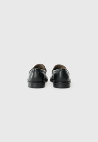 Chaussures en cuir noir avec une finition lisse, des bords arrondis et un talon bas. Vue de dos montrant les détails de couture et un intérieur rembourré.