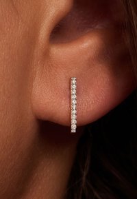 Boucles d'oreilles en argent en forme de barres verticales ornées de petites pierres claires, mettant en valeur un design épuré sur une peau aux tons orangés.