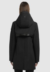 Veste imperméable noire dotée d'une grande capuche, d'un patch logo dans le dos et d'une large bande avec inscription en relief sur le haut du dos.