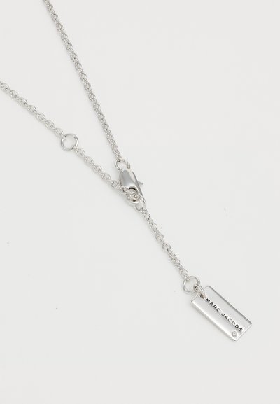 Sølv kædedesignet med et rektangulært mærke, der har "MARJ JACOBS" indgraveret. Glat tekstur, lås med lobster-klik og rund accent.