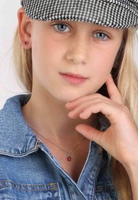 Zilveren hanger met een rode lieveheersbeestje charm, gedragen over een spijkerblouse, met een meisje wiens hand voorzichtig op haar kin rust.